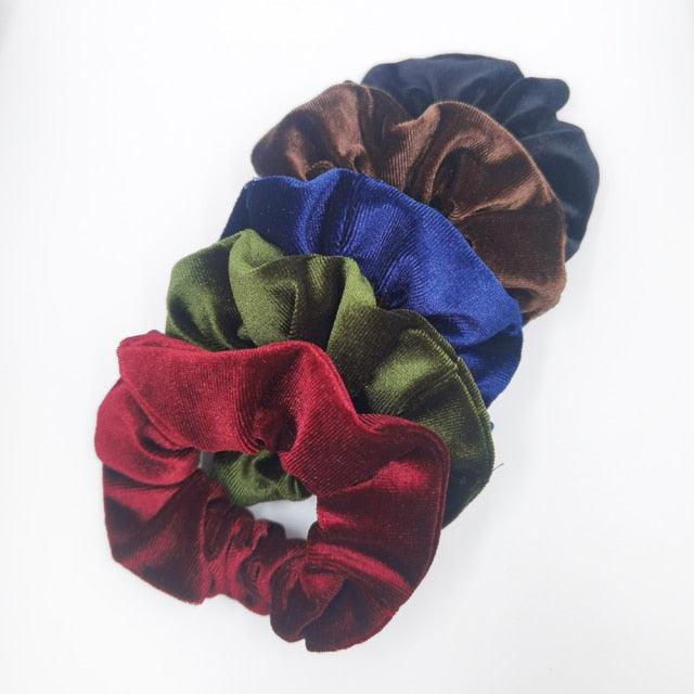 Four velvet scrunchies in red, green, blue, and brown on a white background