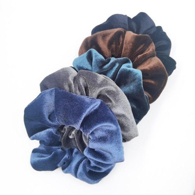 Set of four velvet scrunchies in blue, brown, and gray on a white background