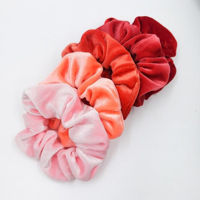 Three velvet scrunchies in red, pink, and orange on a white background