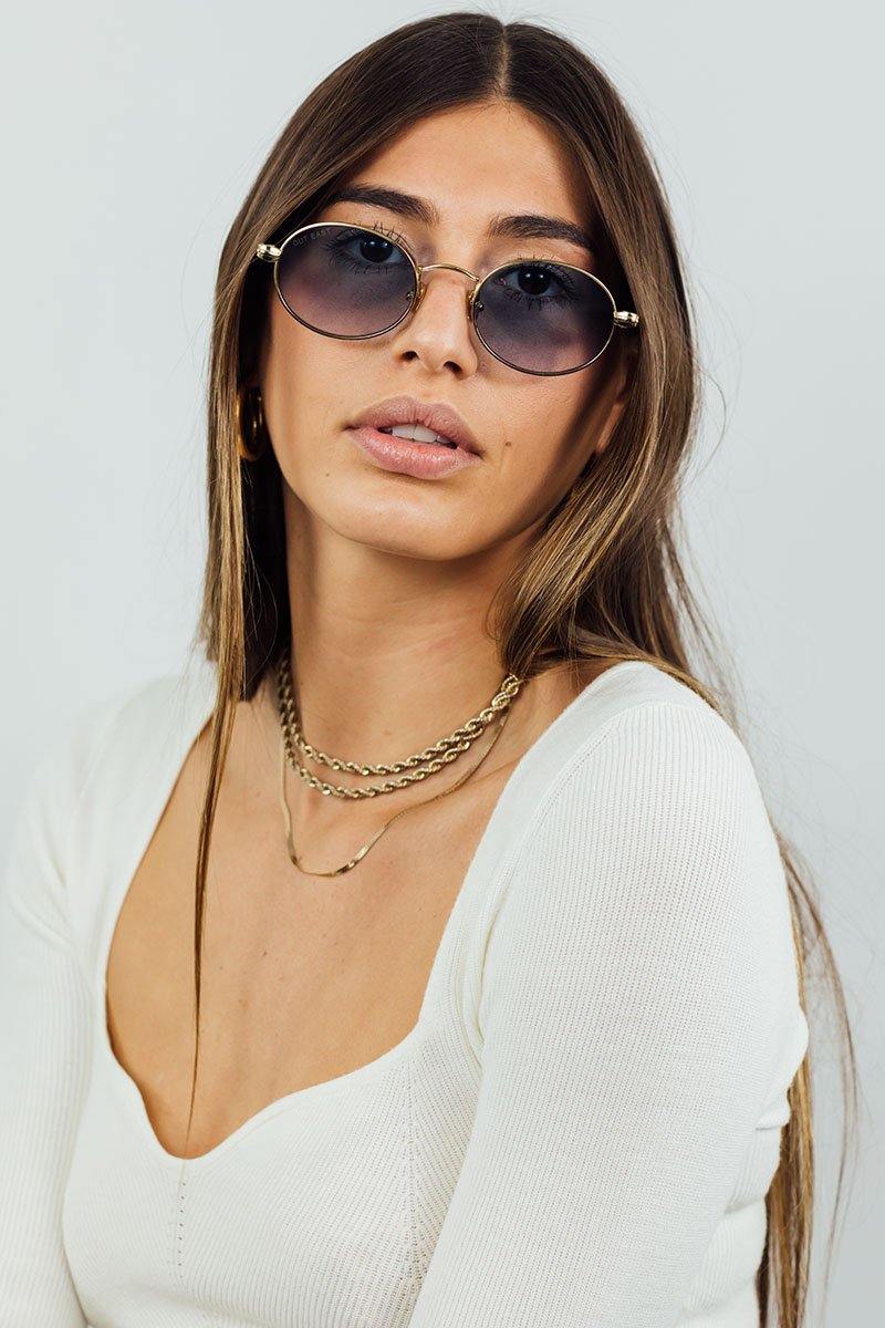 Woman wearing round sunglasses and layered necklaces against a plain background