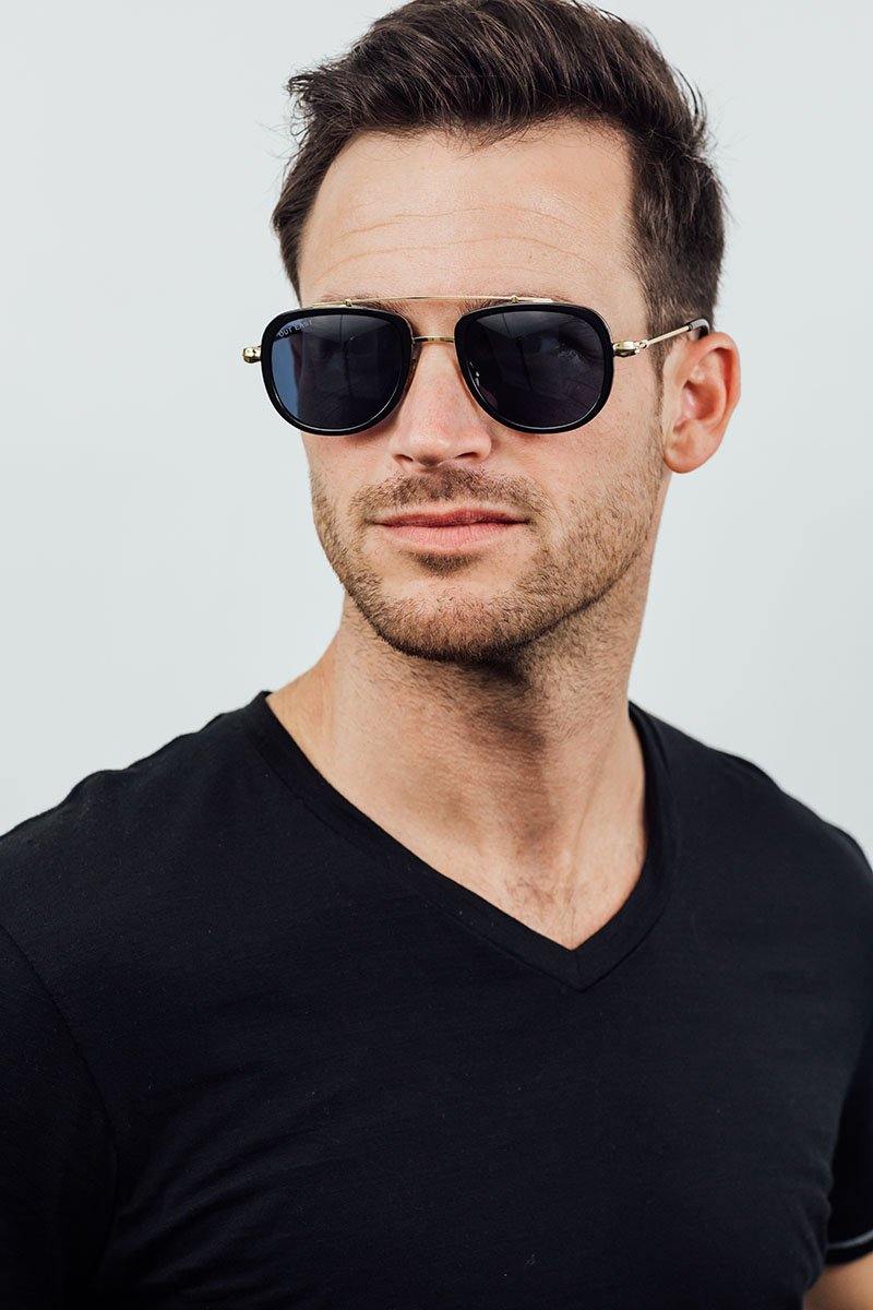 Man wearing dark sunglasses and a black shirt against a light gray background