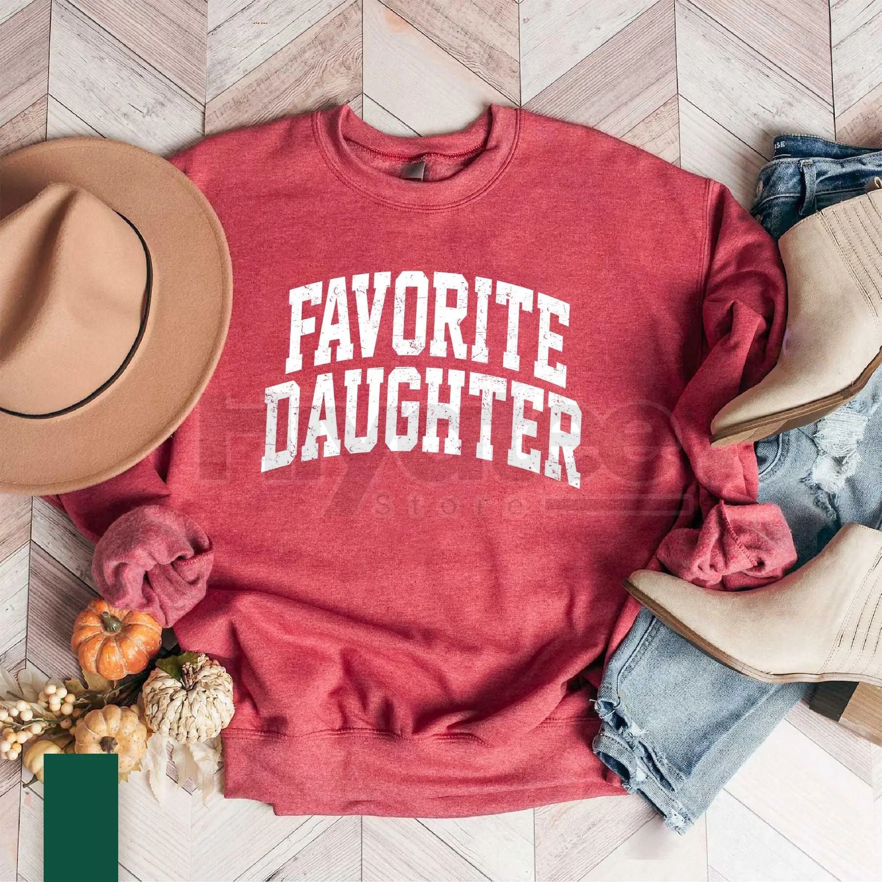 Red sweatshirt with 'Favorite Daughter' text on a wooden floor with fall decor.