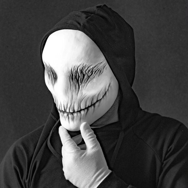 Person wearing a black hooded garment and a white mask with a wide smile and dark eye sockets.