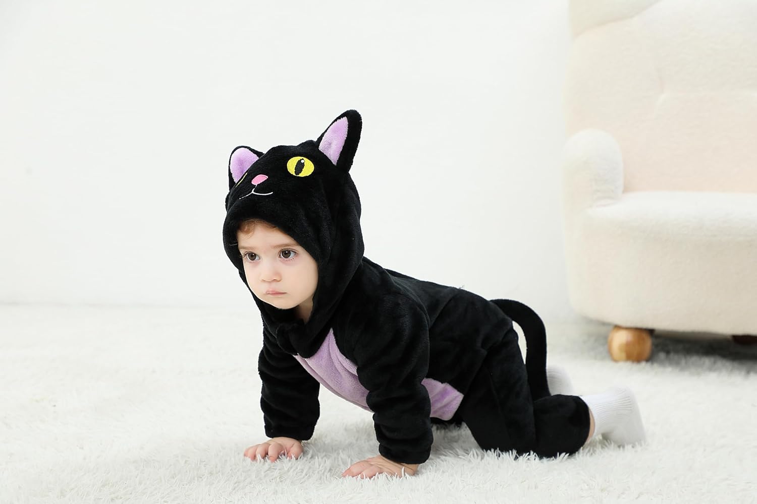 Child wearing a black cat costume on a white carpet