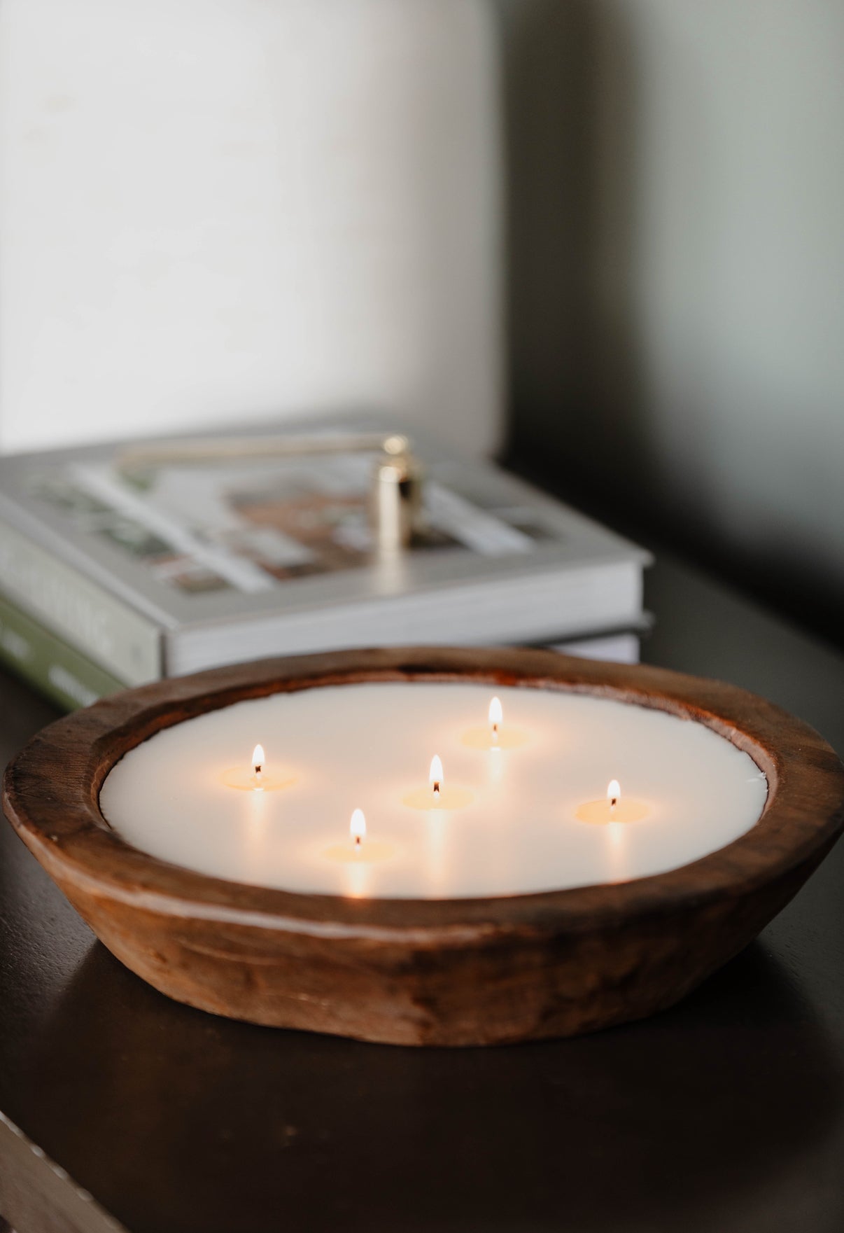 Wooden bowl with multiple lit candles on a dark surface.