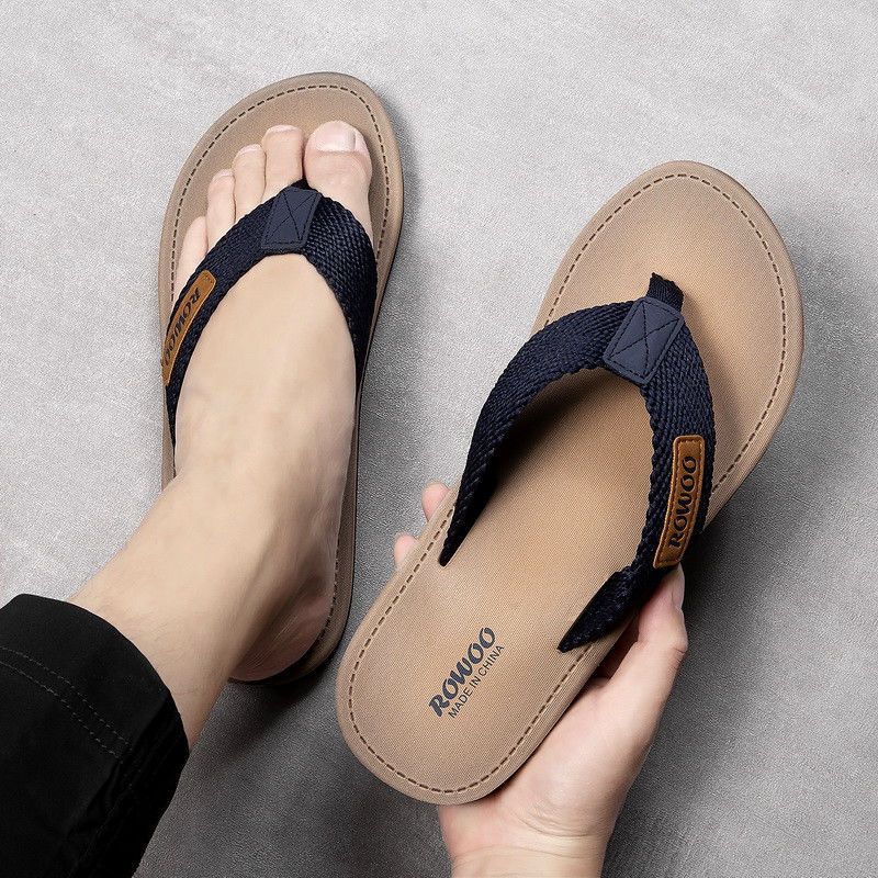Pair of tan sandals with navy straps held by a hand on a gray background