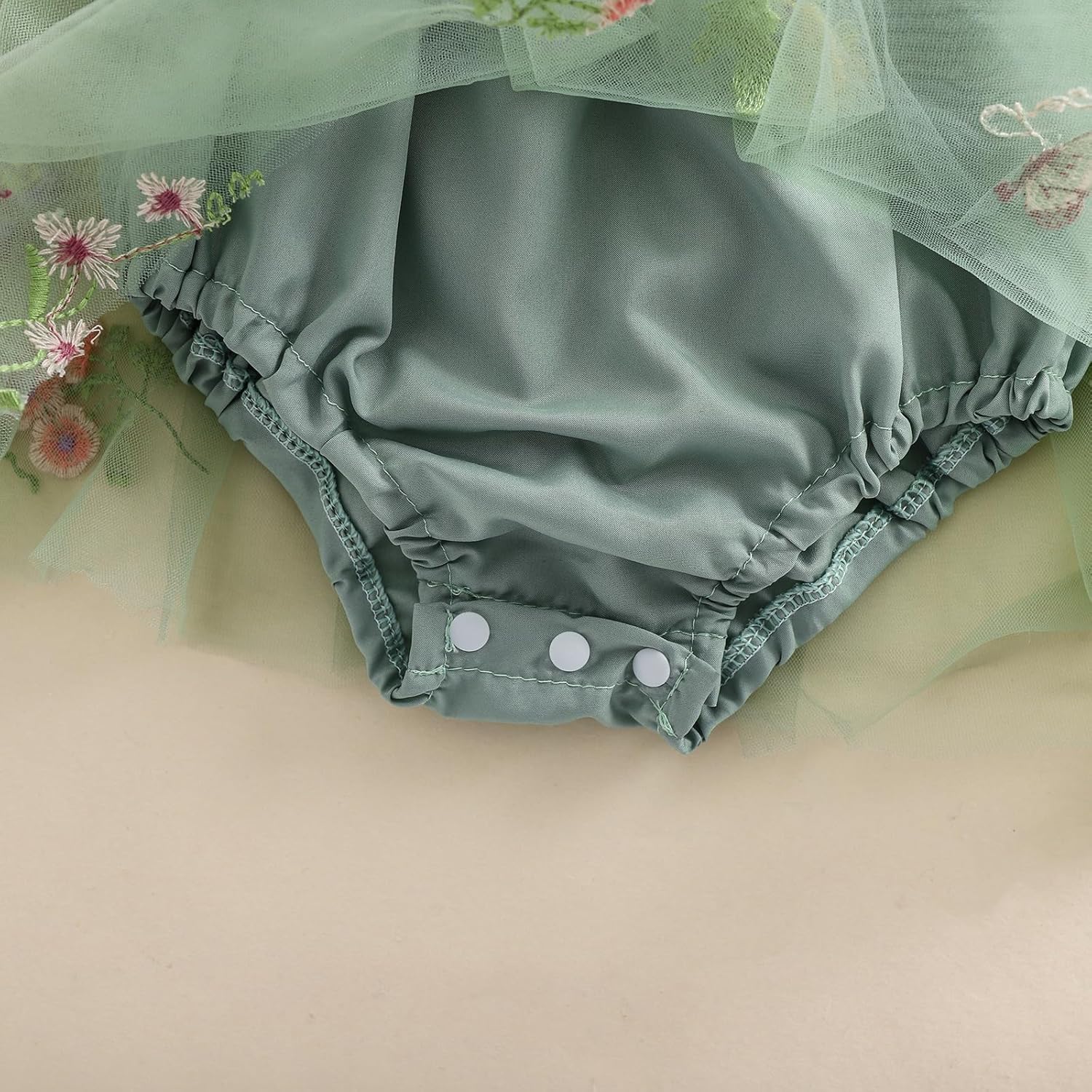 Green baby bloomers with floral embroidery on a beige background