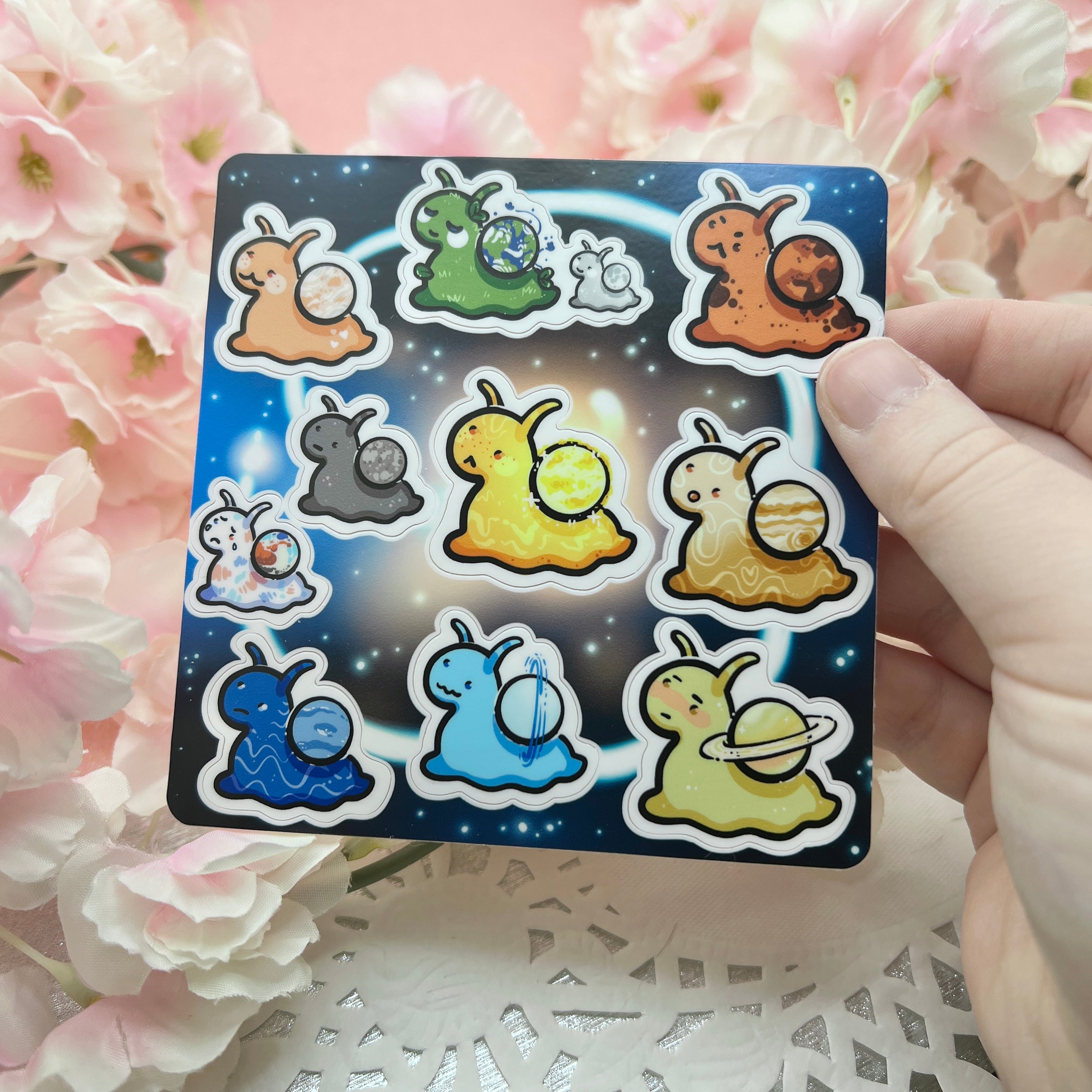 Set of colorful snail-shaped stickers on a card held over pink flowers