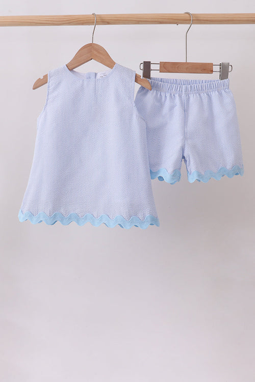 Light blue children's outfit with top and shorts on hangers against a white background