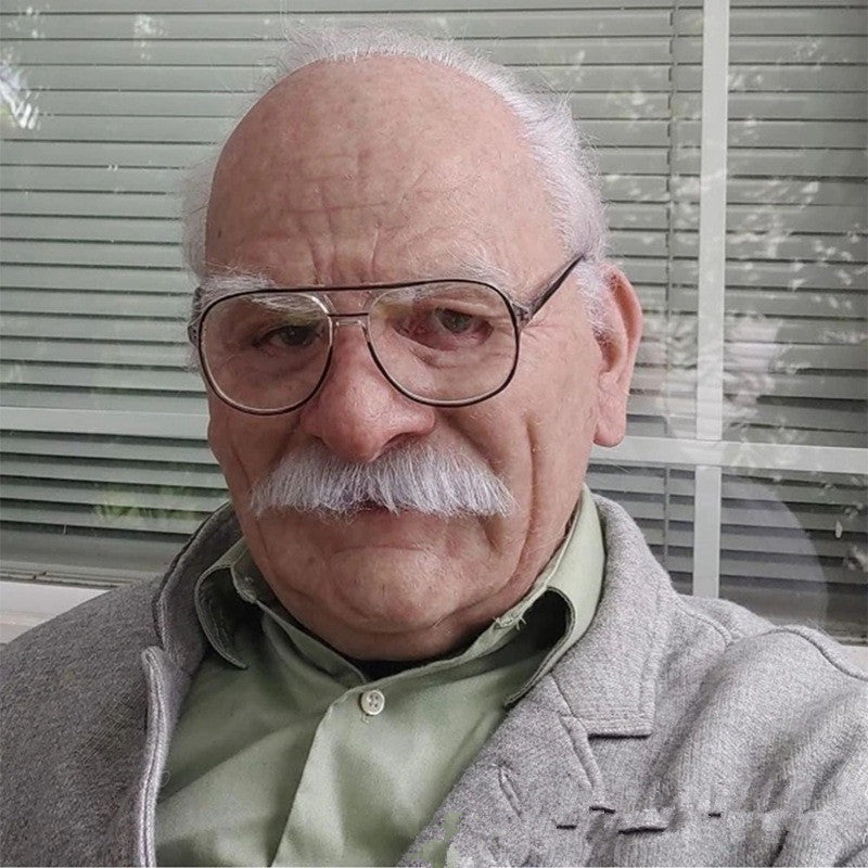 Older man with glasses and a mustache in front of window blinds