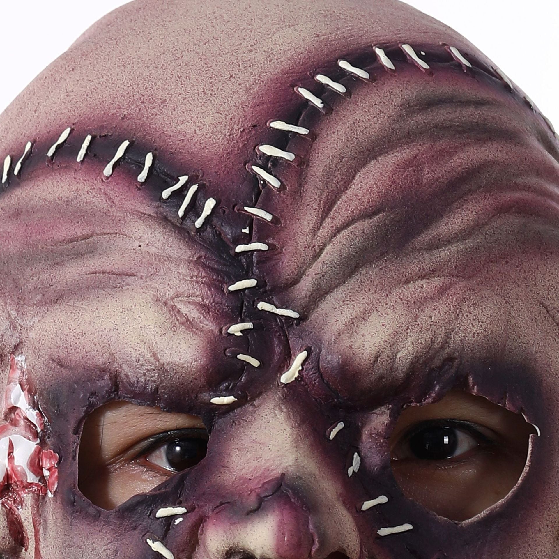 Close-up of a mask with stitched eyes and a bloody nose on a white background