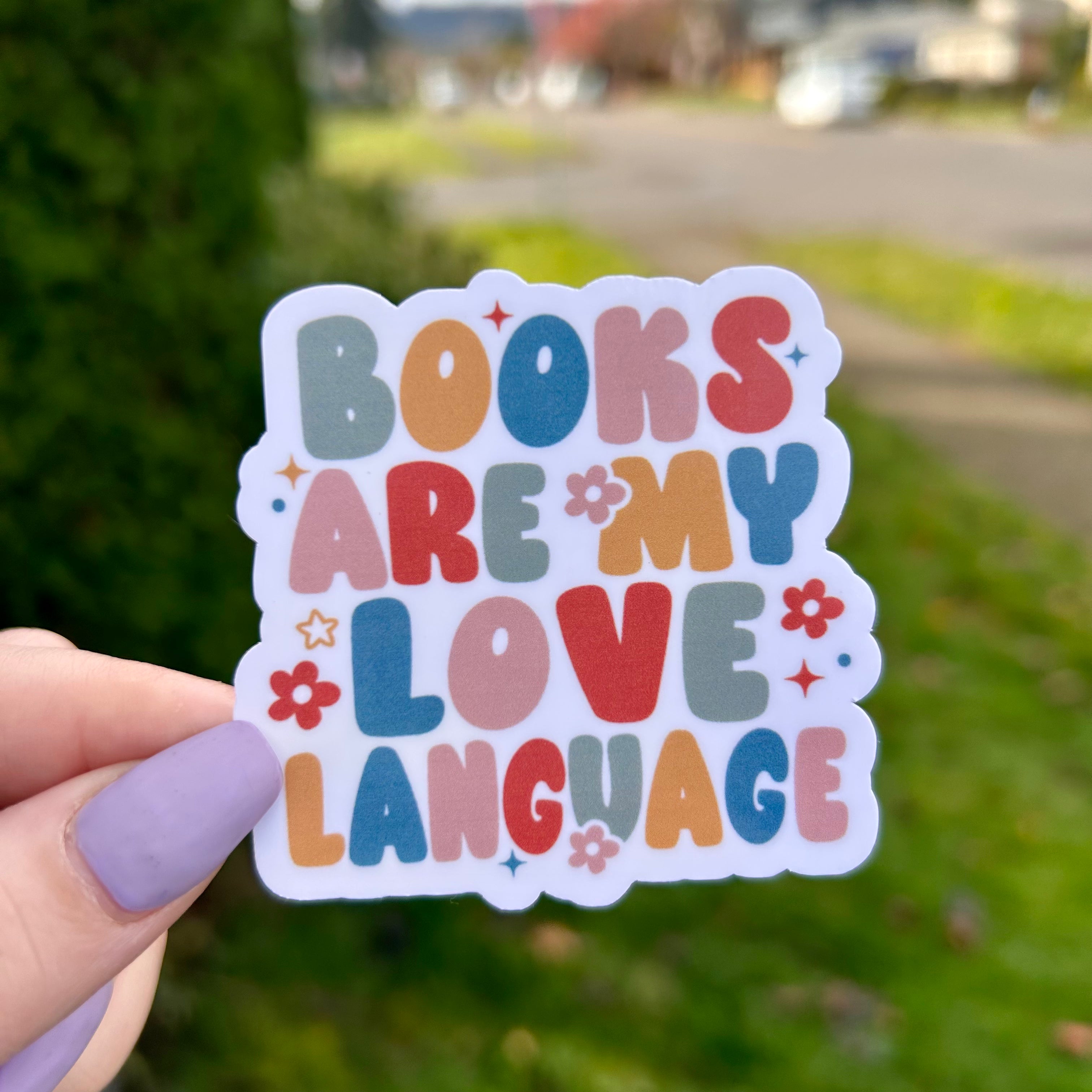 Colorful sticker with 'Books are my love language' text held by a hand outdoors.