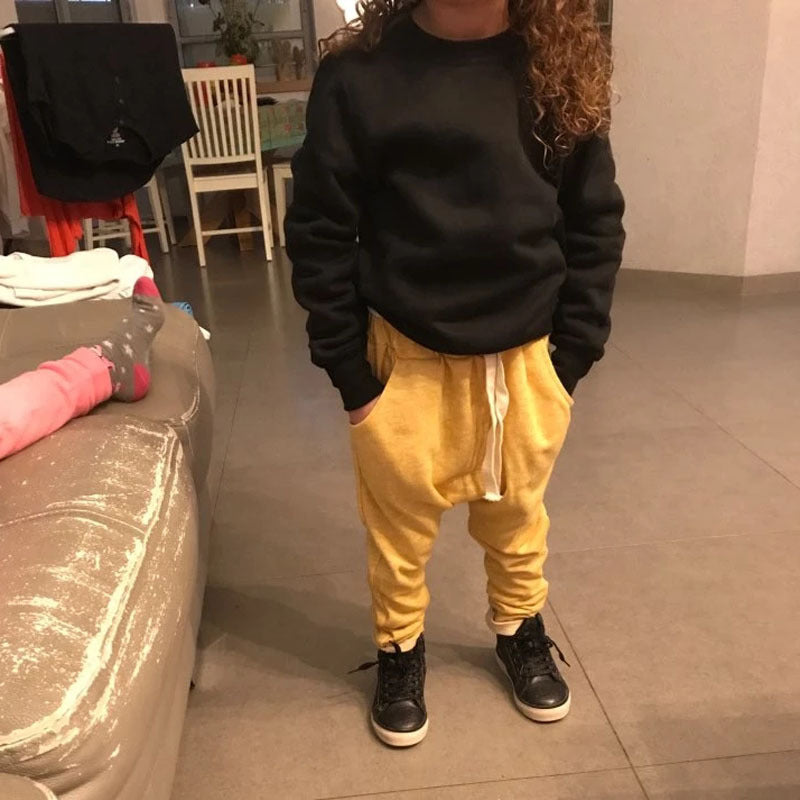 Person wearing a black sweatshirt and yellow pants standing in a room with a couch and chair.