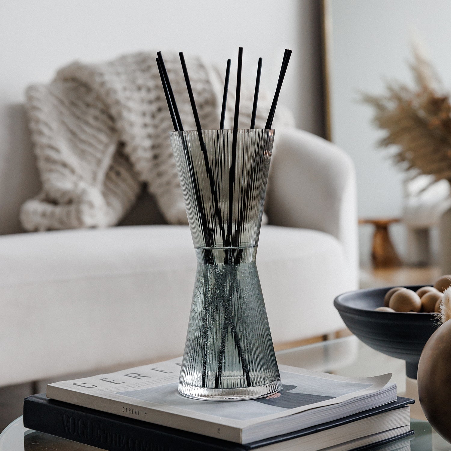 A glass diffuser with black sticks on a stack of books in a living room setting.