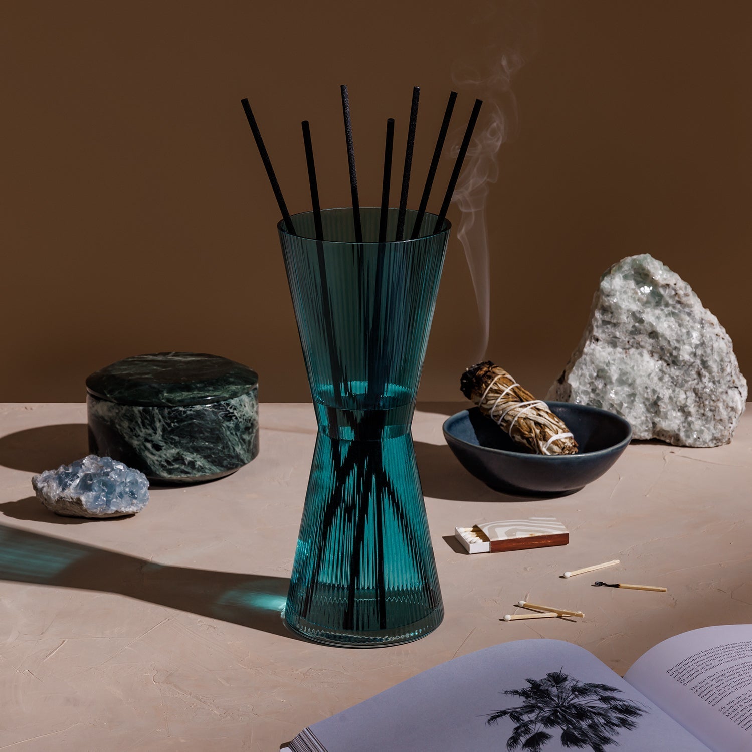 Teal diffuser with black sticks on a table with crystals and matches