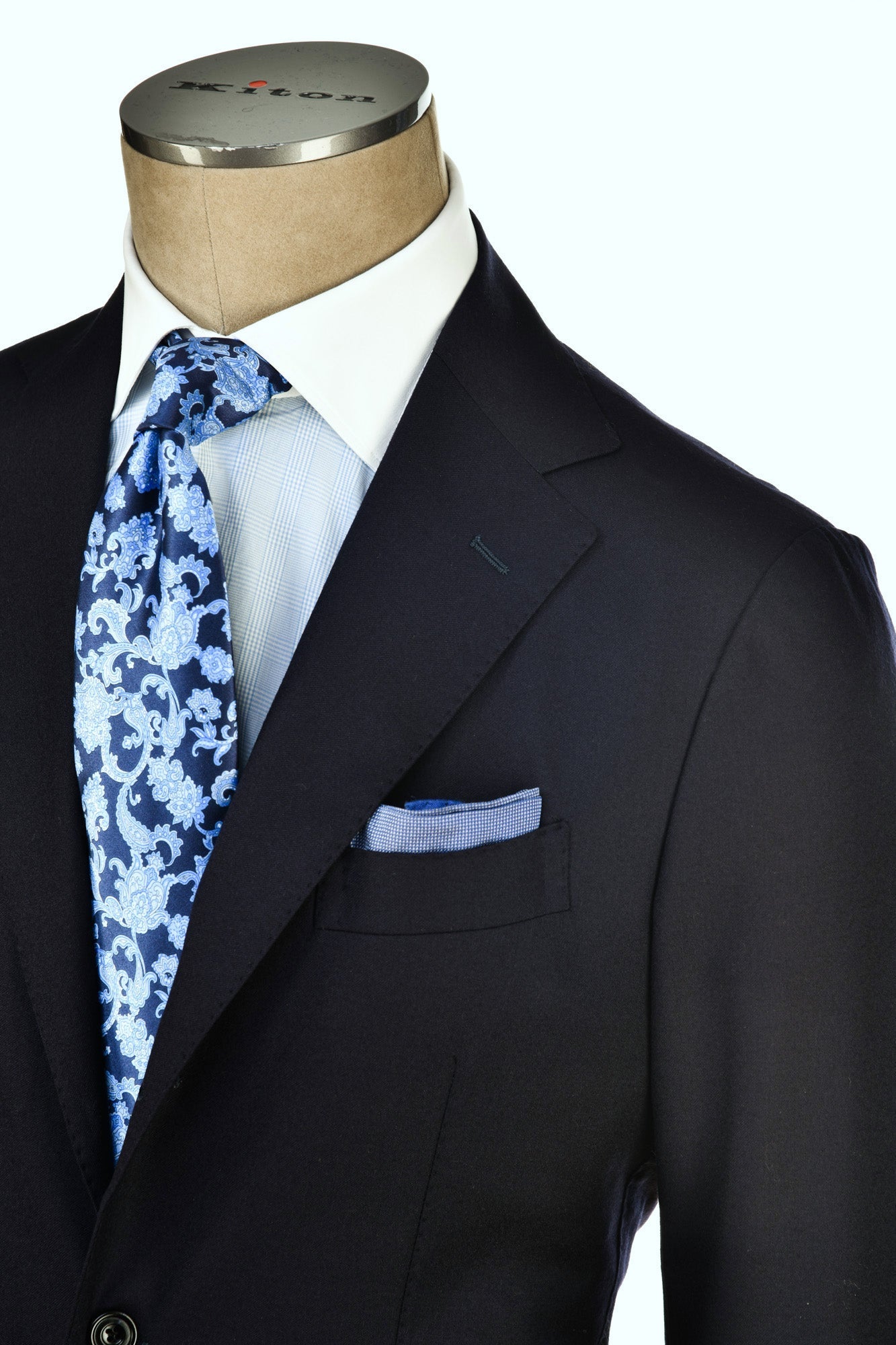 Black suit jacket with a white shirt, blue patterned tie, and matching pocket square on a mannequin.
