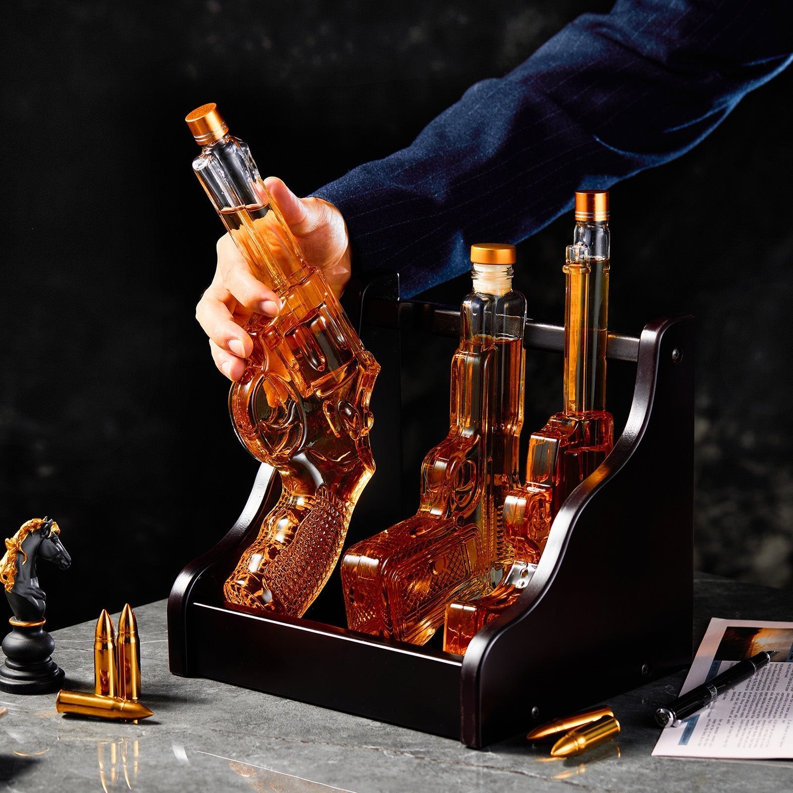 Decorative bottle holder with glass bottles shaped like guns on a dark surface.