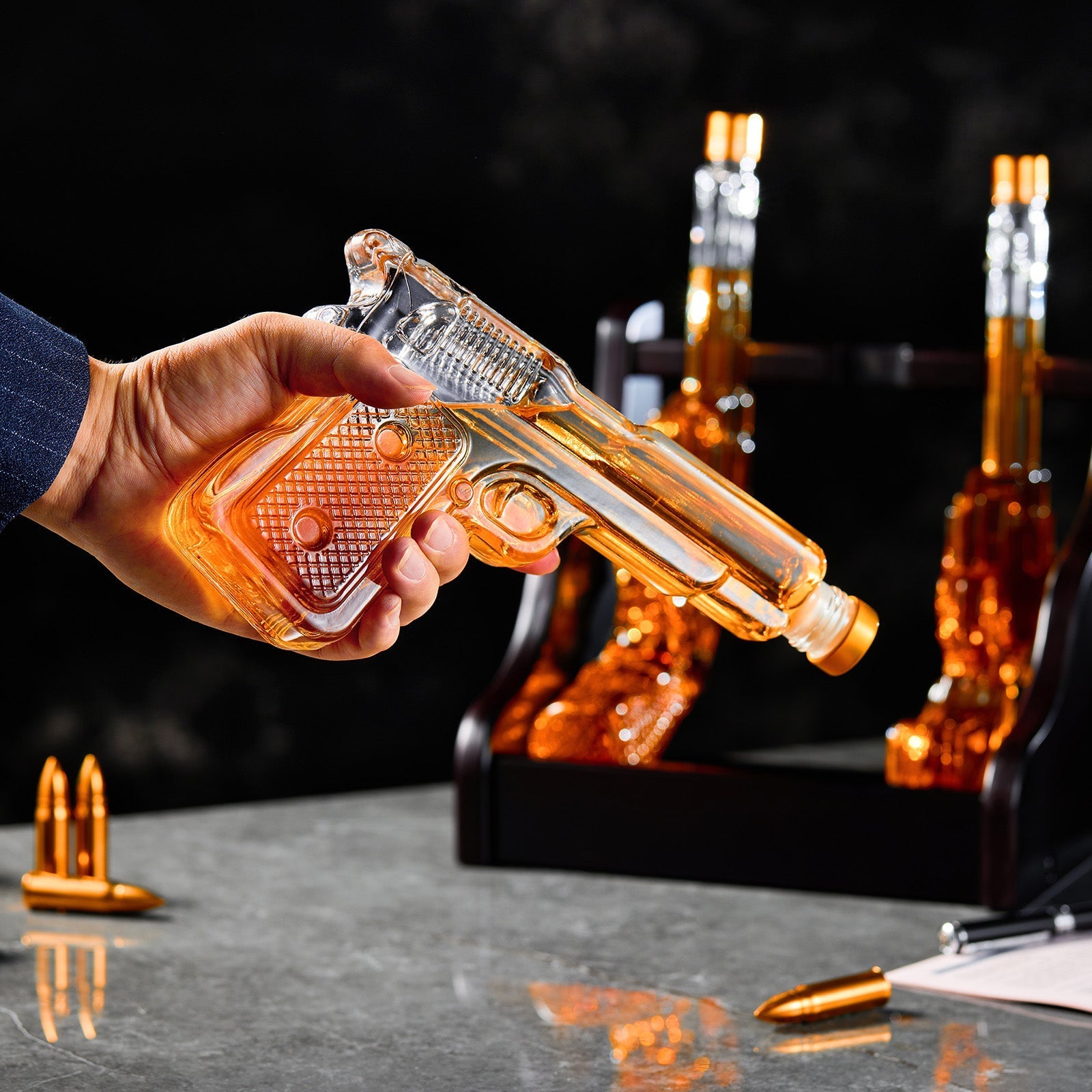 Glass gun-shaped bottle being held with a dark background and additional bottles in the background.