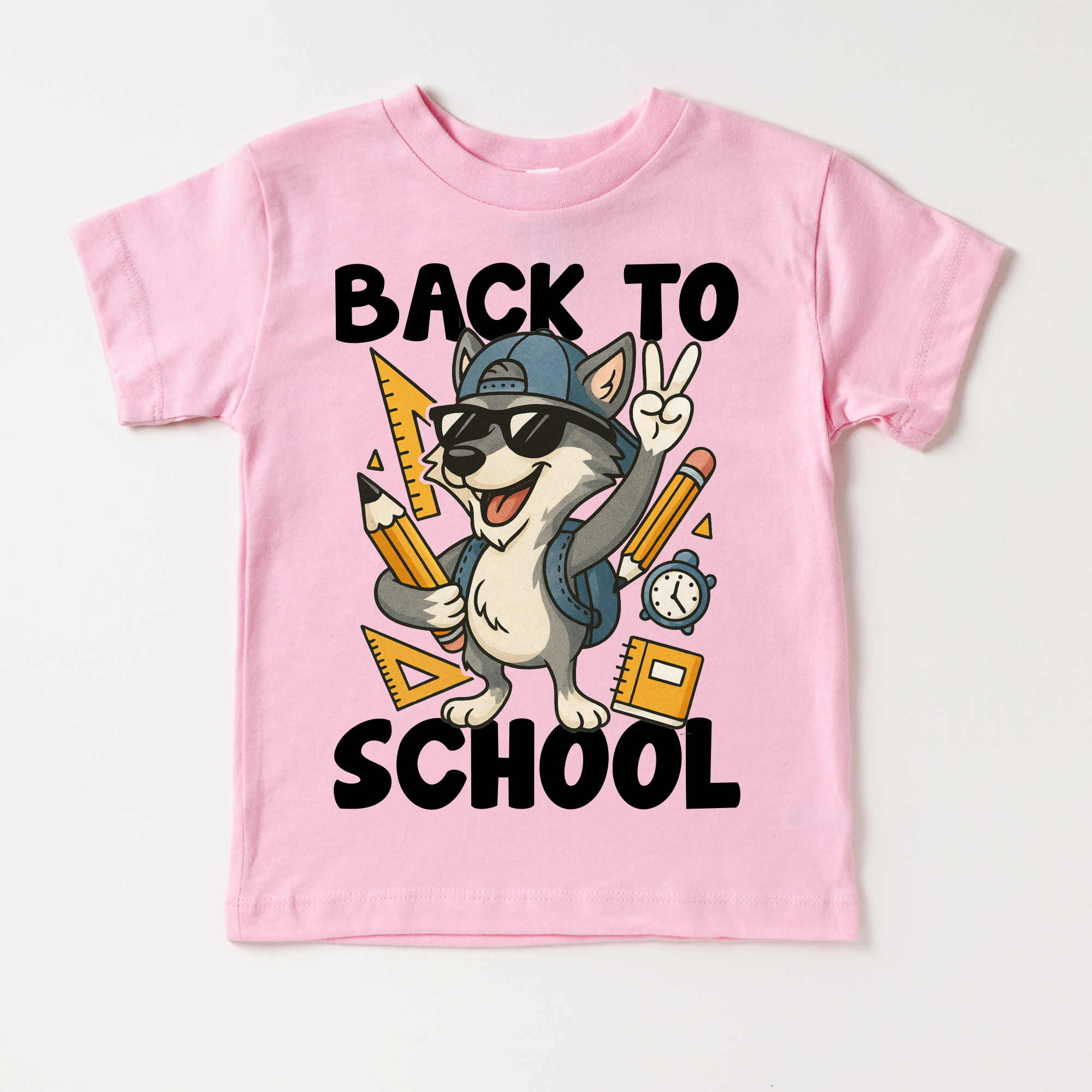 Pink t-shirt with a cartoon wolf wearing sunglasses and a cap, holding pencils and a ruler, with 'Back to School' text on a white background.