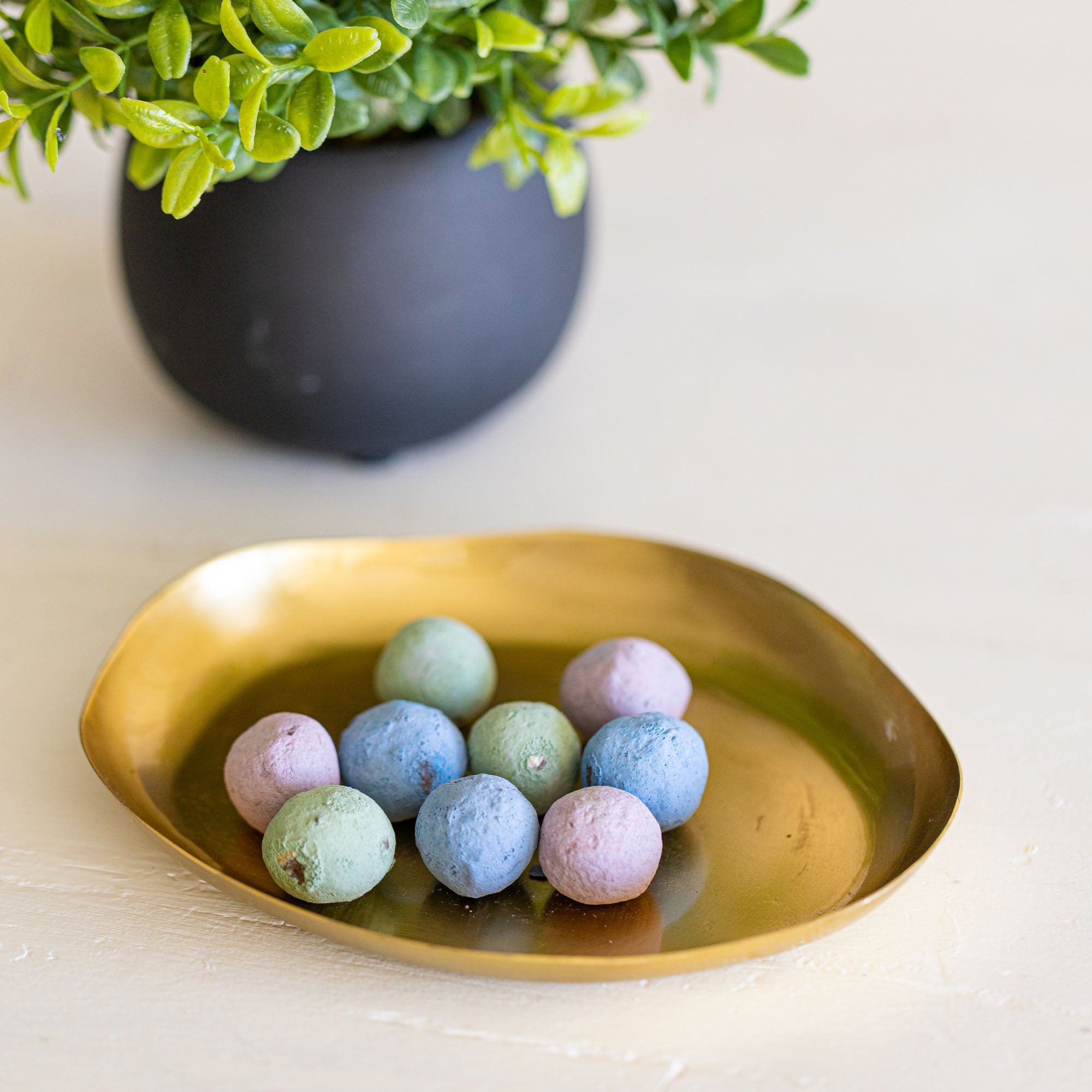 Pastel-colored bath bombs on a gold dish with a plant in the background