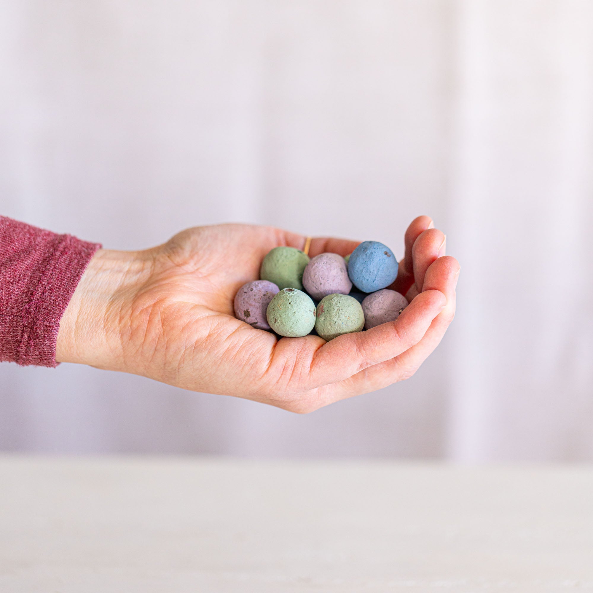 Hand holding pastel-colored seed balls against a plain background