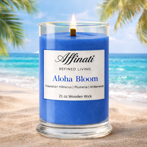 Blue candle labeled 'Aloha Bloom' by Affinati on a beach with palm trees and ocean in the background