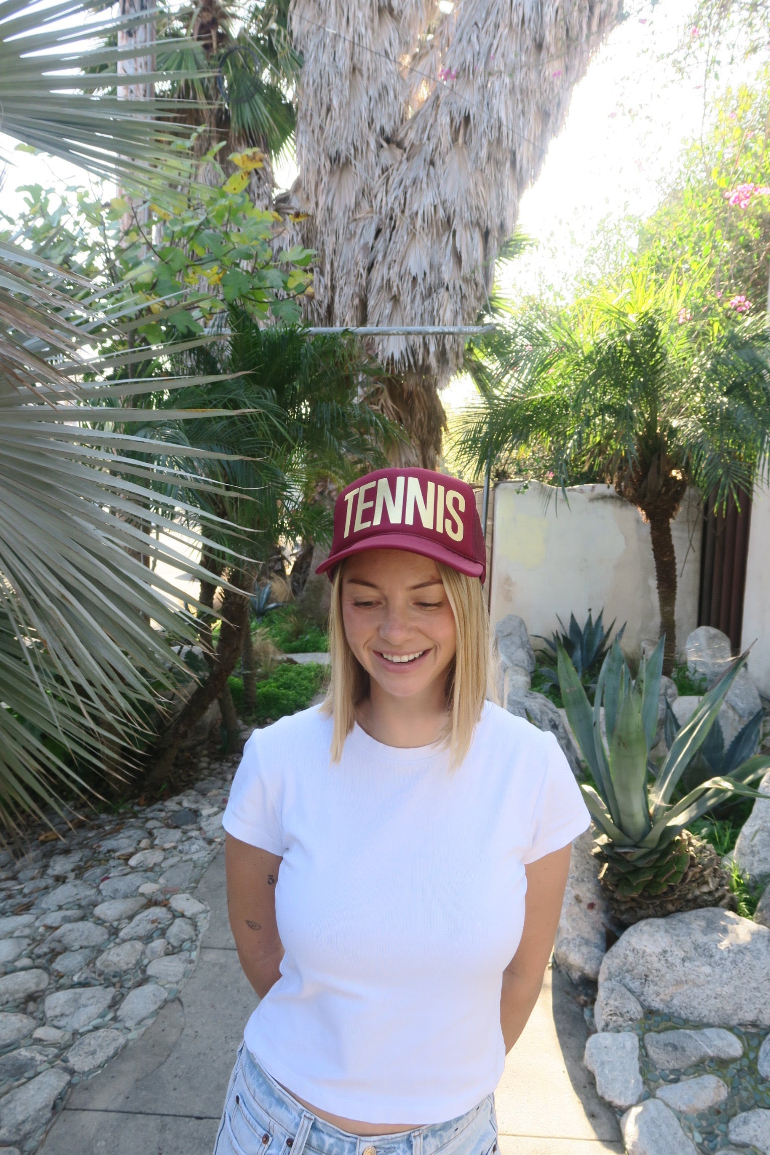 Person wearing a red 'Tennis' cap in a garden setting
