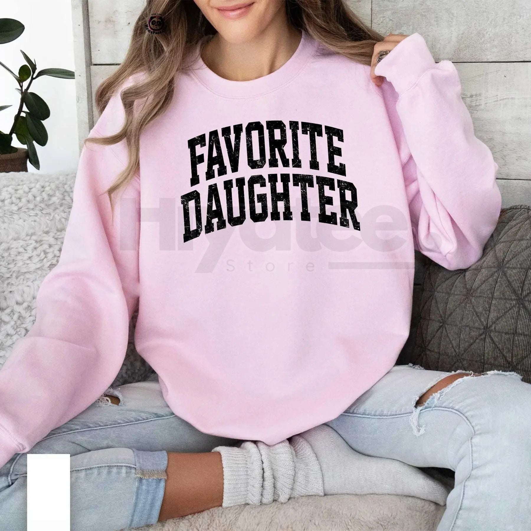 Person wearing a pink sweatshirt with 'FAVORITE DAUGHTER' text, sitting on a couch.