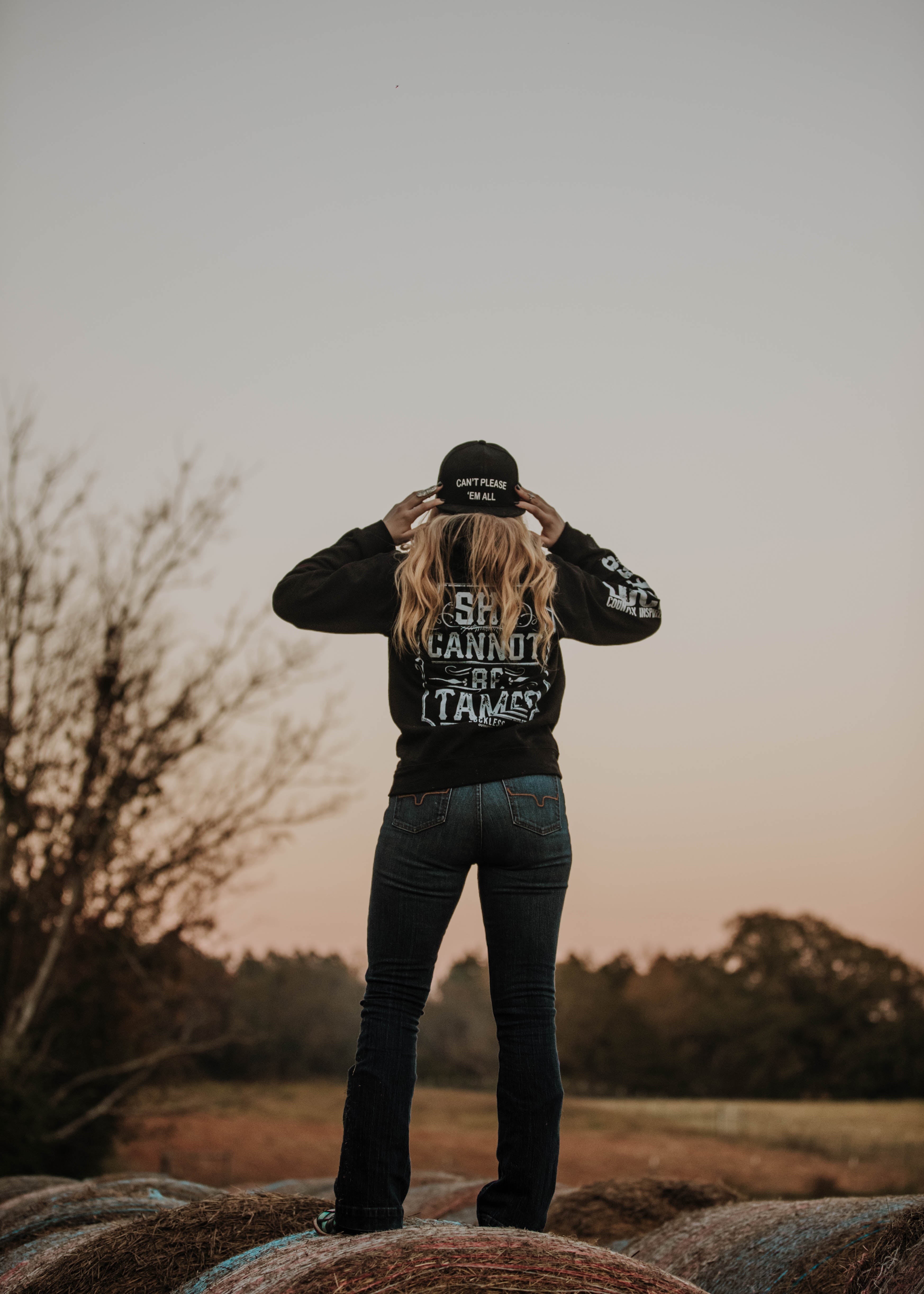 Person wearing a black jacket with text, standing outdoors with a sunset background