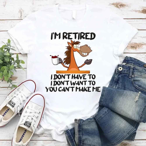 White t-shirt with a cartoon horse graphic and text, paired with jeans and sneakers on a wooden surface.