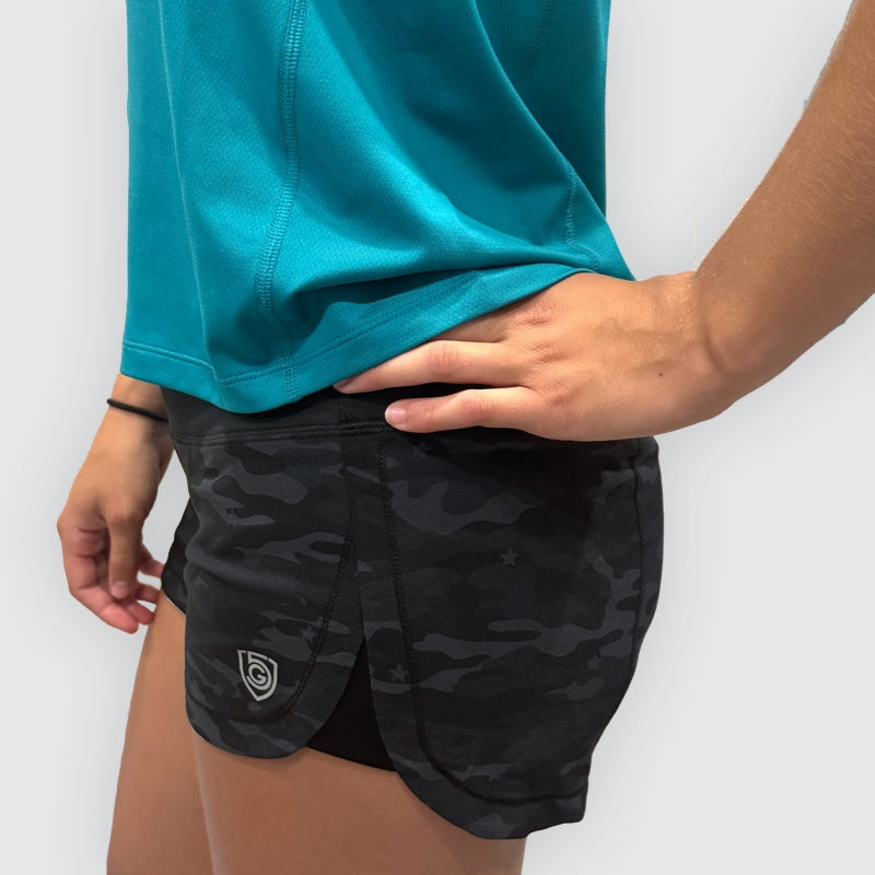 Person wearing black camouflage shorts with a logo on a white background