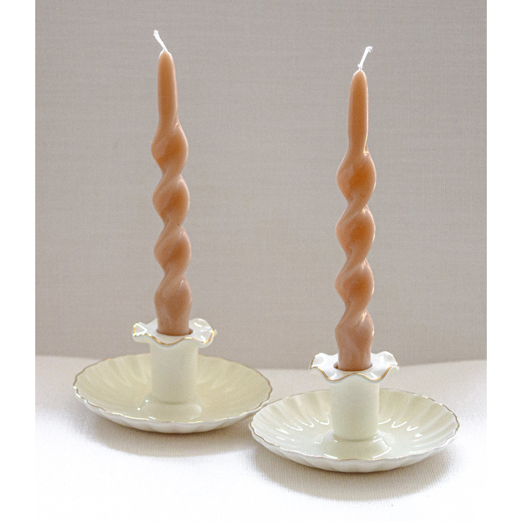 Two twisted candles on decorative candle holders against a plain background