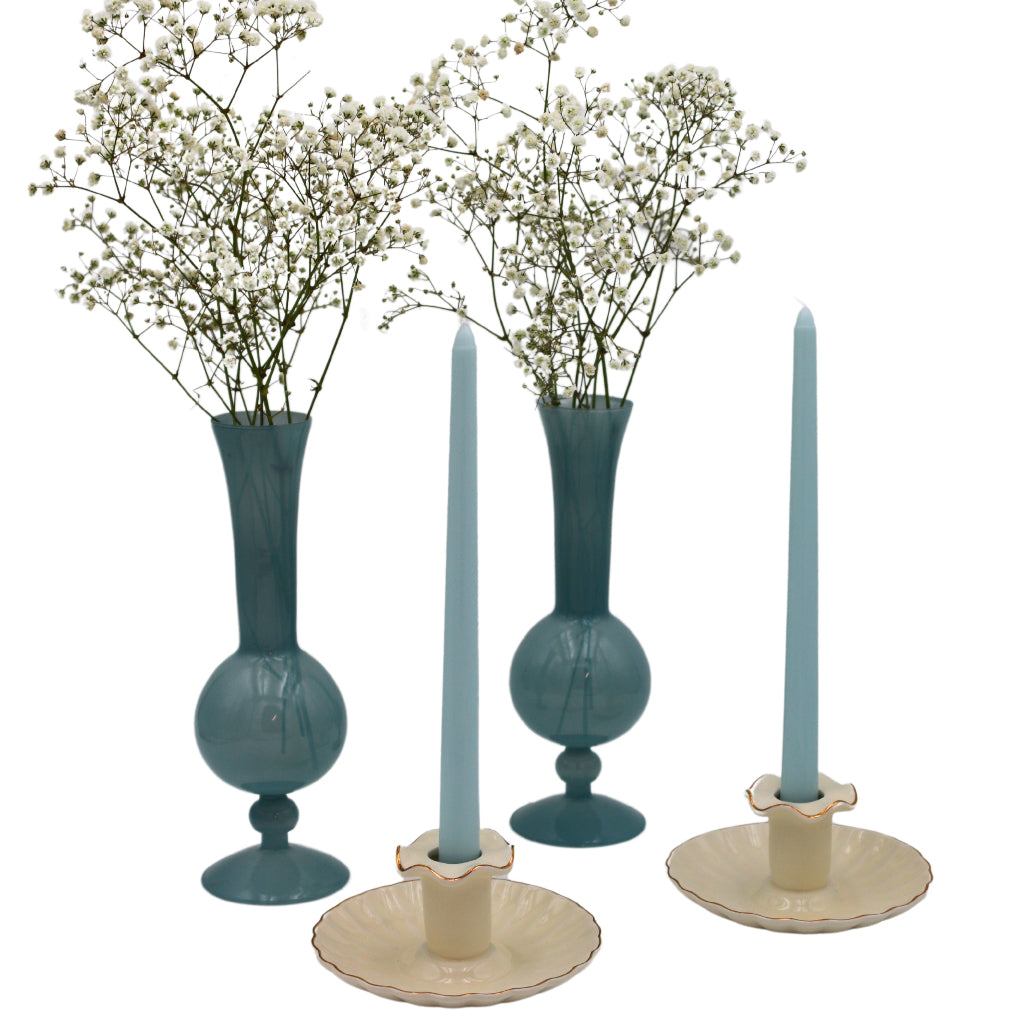 Two teal vases with white flowers and two blue candles in ceramic holders on a white background