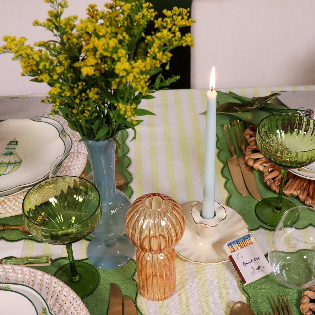 Dining table setting with green glassware, yellow flowers, and a lit candle.