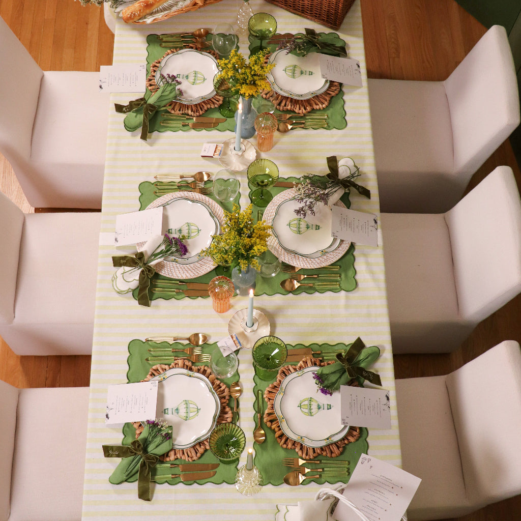 Dining table set with place settings, green placemats, and centerpieces.