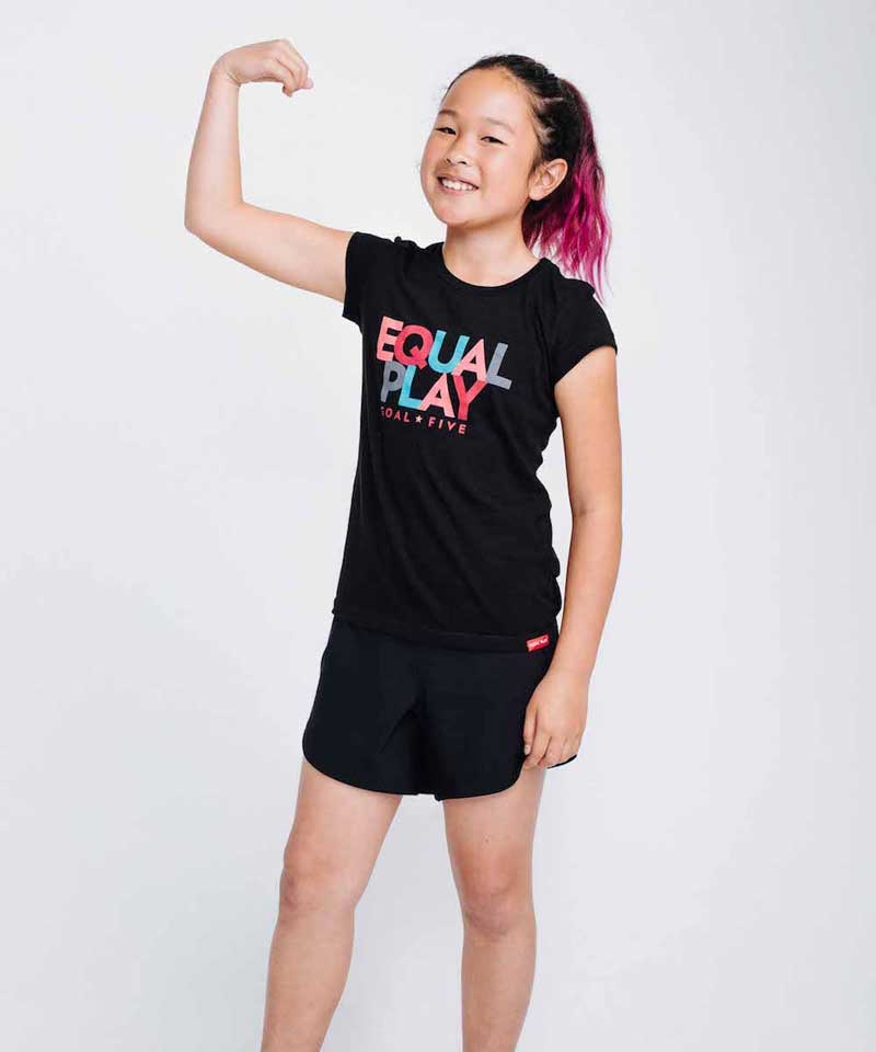 Young girl flexing her arm wearing a black 'Equal Play' t-shirt on a white background