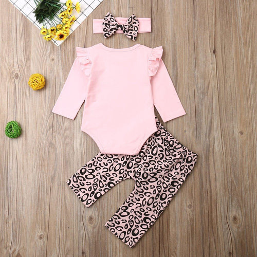 Baby outfit with pink long-sleeve bodysuit, leopard print pants, and headband on a wooden surface.