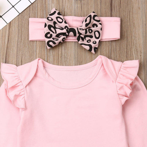 Pink baby romper with ruffled sleeves and a matching headband with leopard print bows on a wooden surface.