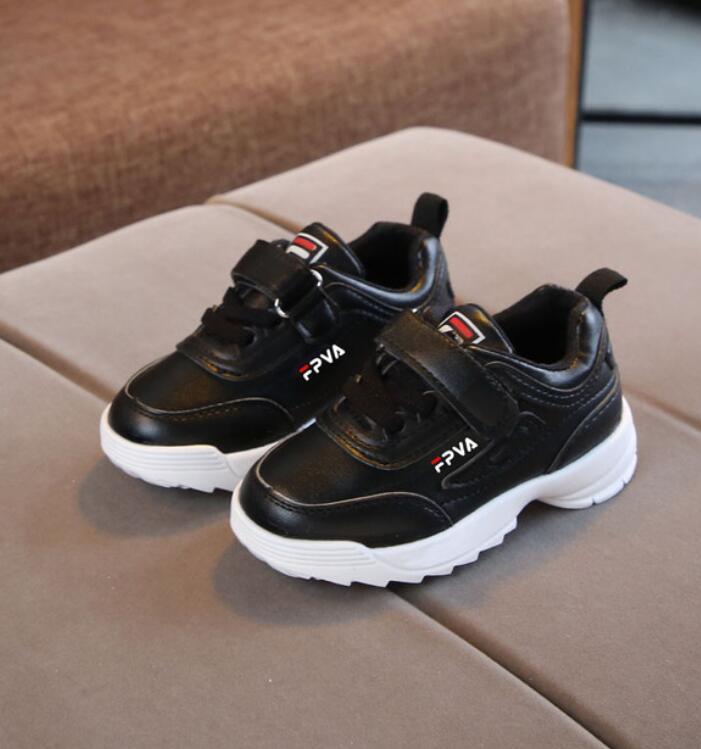 Pair of black children's sneakers with white soles on a brown surface