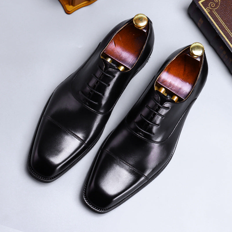 Pair of black dress shoes with brown soles on a light gray background