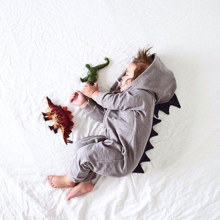 Child wearing a dinosaur onesie with toy dinosaurs on a white background