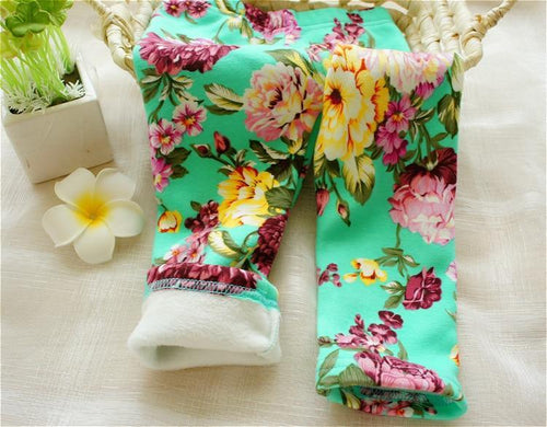 Floral-patterned leggings on a light surface with a plant and flower in the background