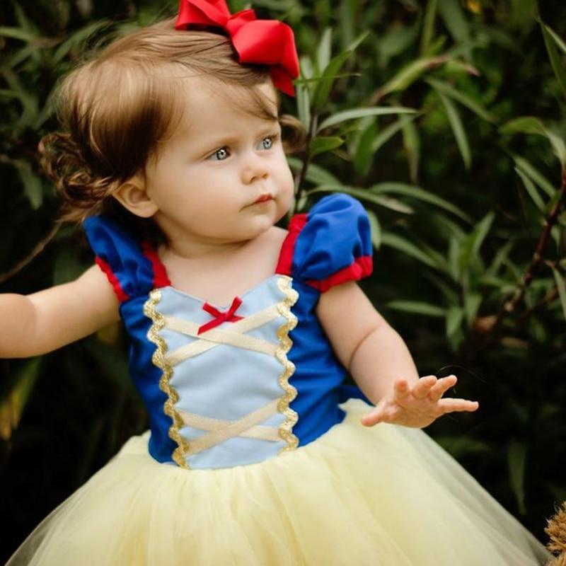 Child in a Snow White costume with a red bow against a green leafy background