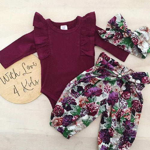 Baby outfit set with burgundy romper, floral pants, and headband on a light wooden surface.
