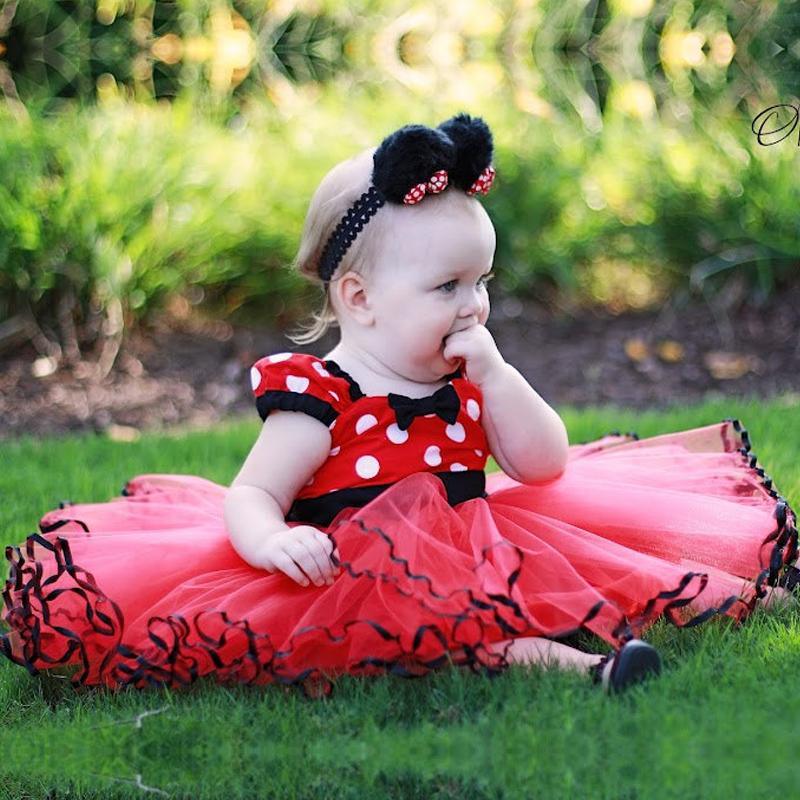 Baby in a red polka dot dress sitting on grass