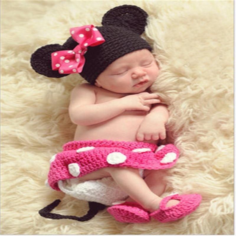 Newborn baby wearing a black and pink crochet outfit with mouse ears and bow on a soft beige surface.