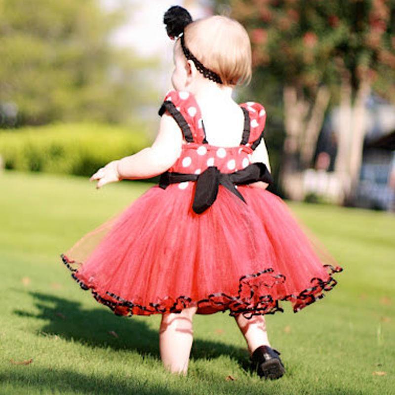 Child in a red polka dot dress with black accents running on grass