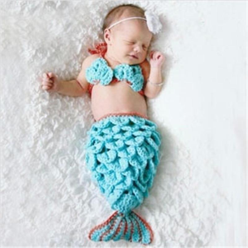 Baby in a turquoise mermaid costume lying on a white textured surface