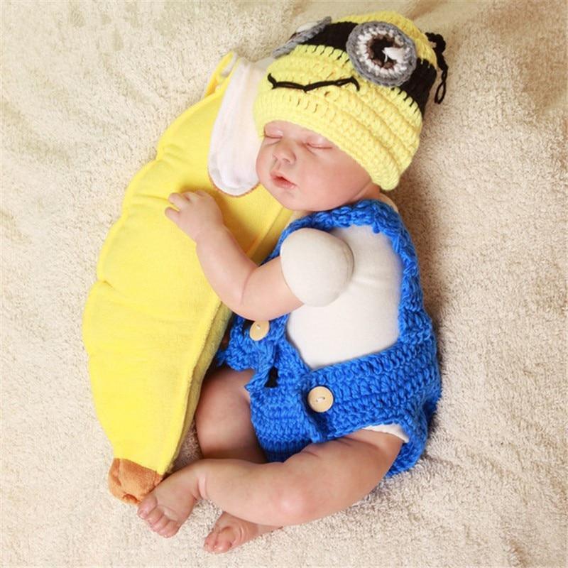 Newborn baby in a Minion costume with a yellow banana and blue outfit on a beige surface.