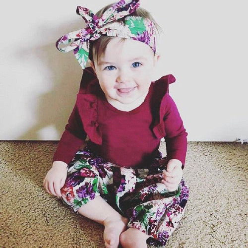 Child wearing a maroon outfit with floral patterns sitting on a carpeted floor.